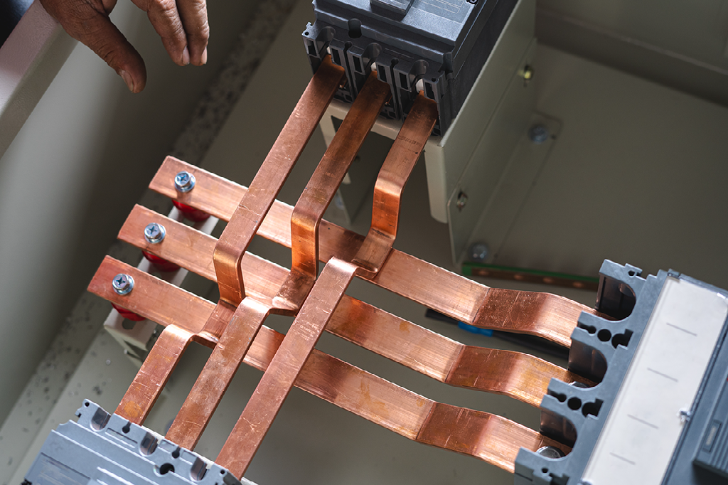 A technician's hand pointing to copper busbars wired inside an electrical panel